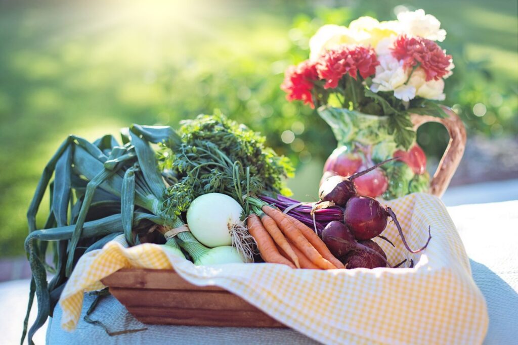 Legumes e verduras em um cesto, sobre uma mesa em um jardim.